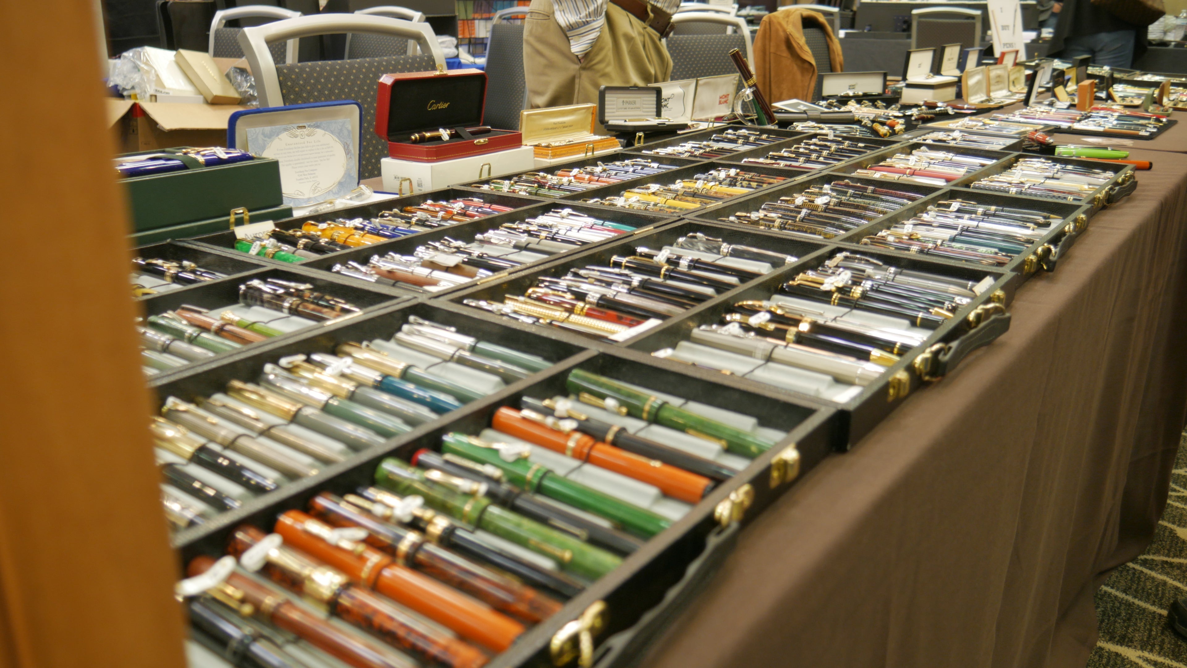 Table displaying various pens and writing instruments at a convention.